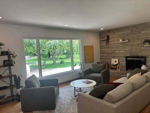 Living room with stone fireplace and large backyard window