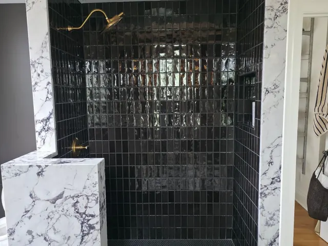 Walk-in shower with dark tile and marble-look surround