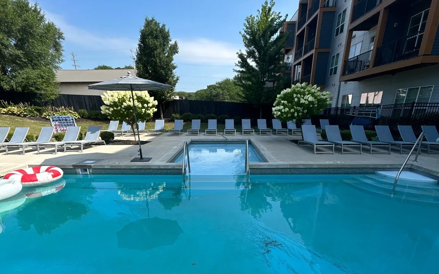 Renovated apartment community pool courtyard with lounge chairs, a shallow entry spa with handrails, and a multi-story residential building