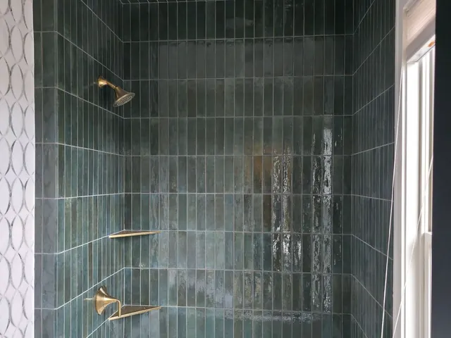 Bathroom tub surround with dark green tile and brass fixtures